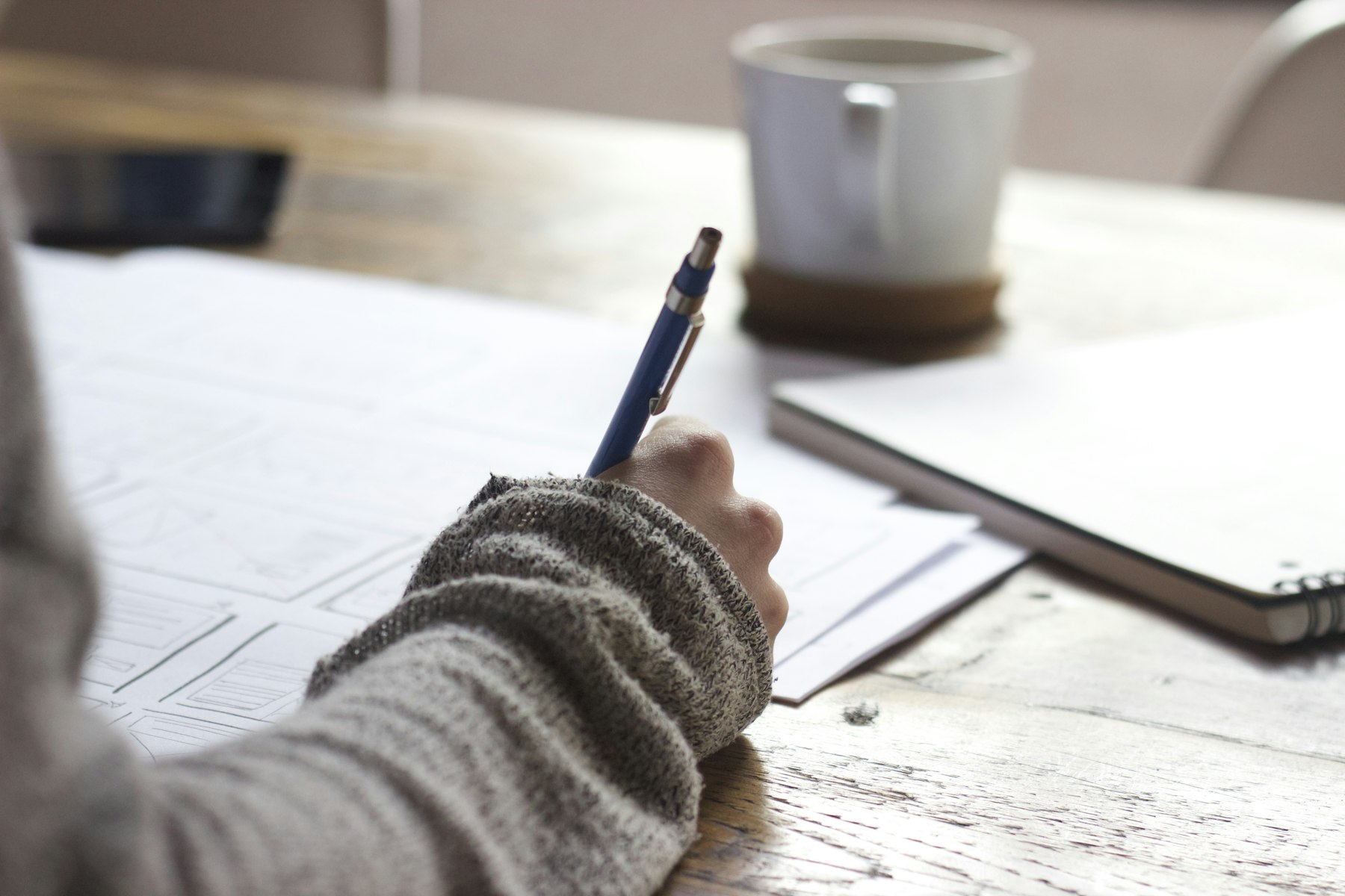 Una persona escribe en un cuaderno, con café al lado